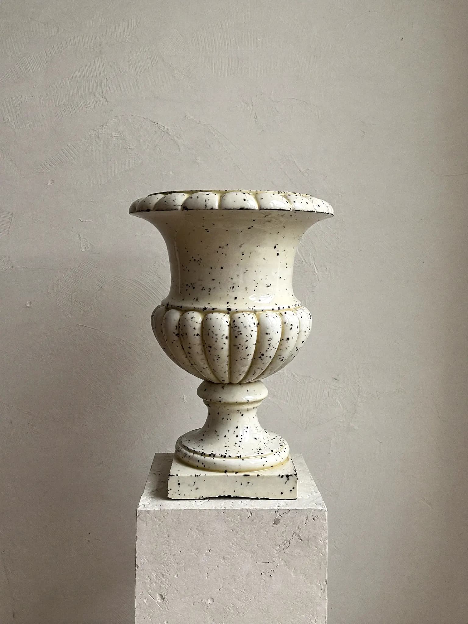 Footed Urn stoneware planter in iron speckle glaze, on a stone block against a plaster wall