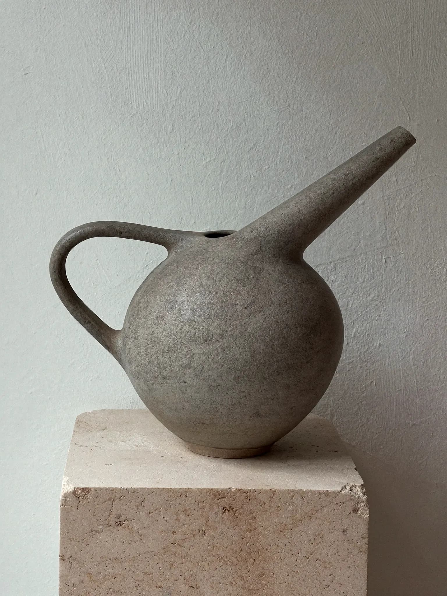 Pour Bottle stoneware piece in ash grey glaze, on a stone block against a plaster wall