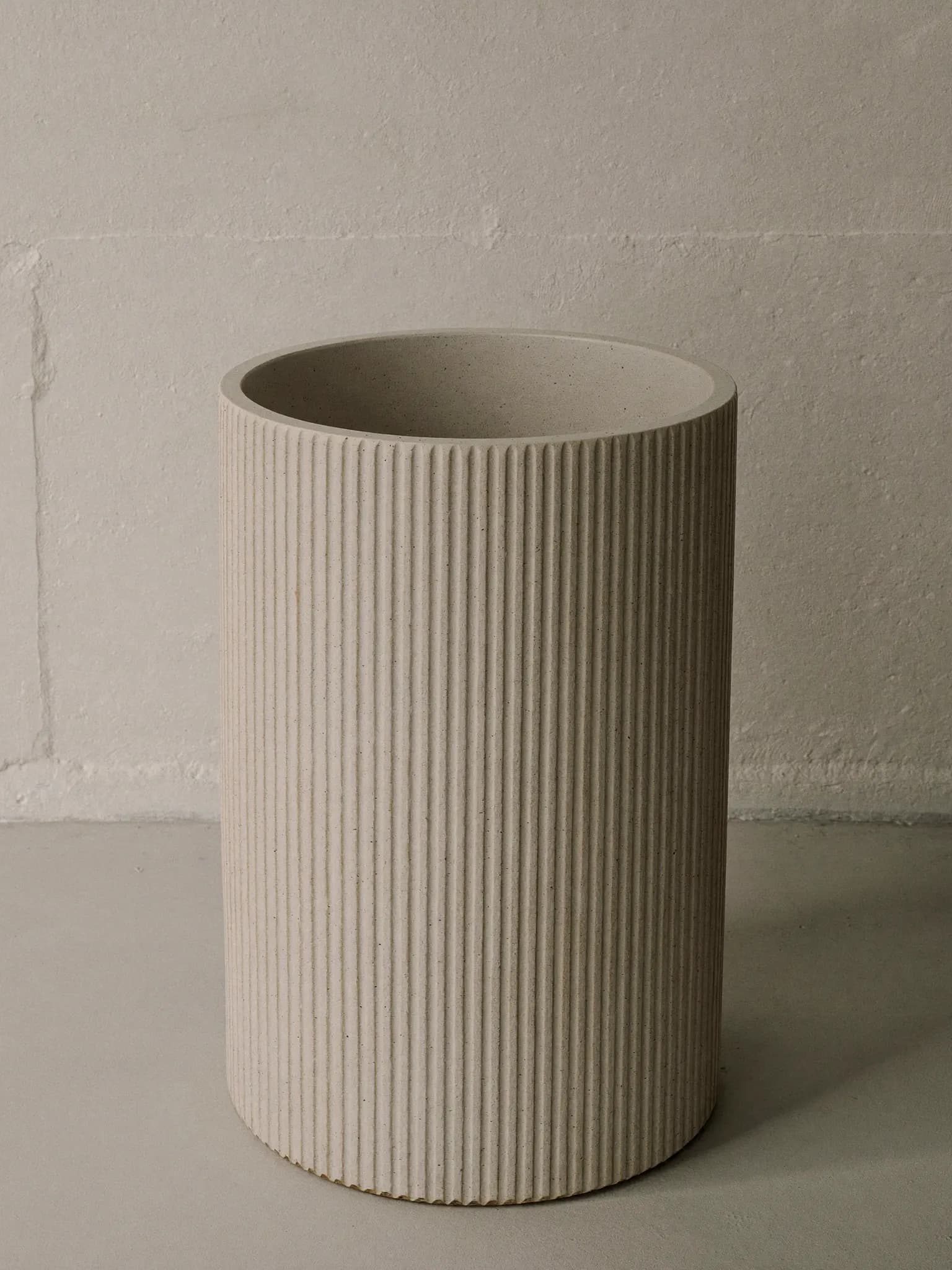 Big Ridge stoneware planter in oat matte glaze, on a stone block against a plaster wall